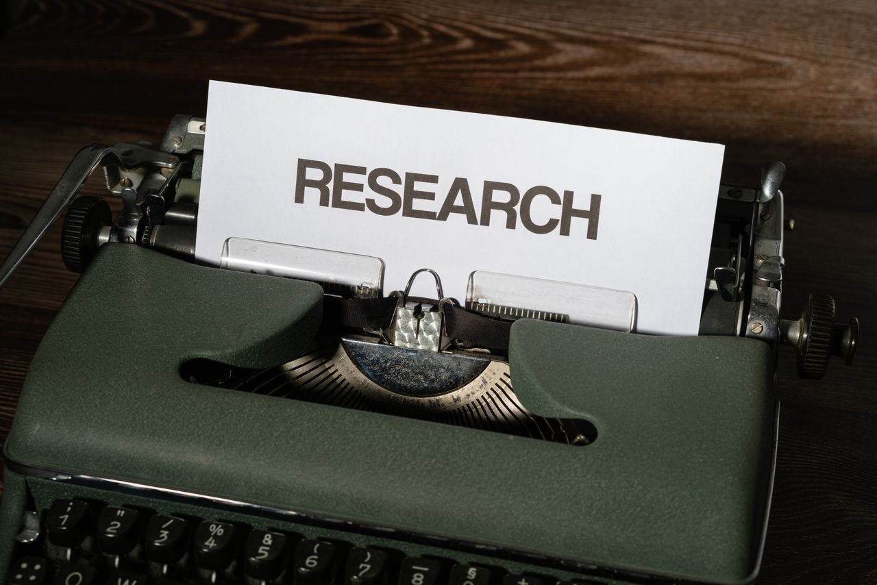 Close-up of a vintage typewriter with a paper labeled 'Research' inserted, on a wooden surface.